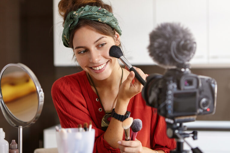 Portrait of beautiful smiling female vlogger makes video review, uses cosmetic product, records useful content for blog online. Successful woman blogger works on improvement social networking